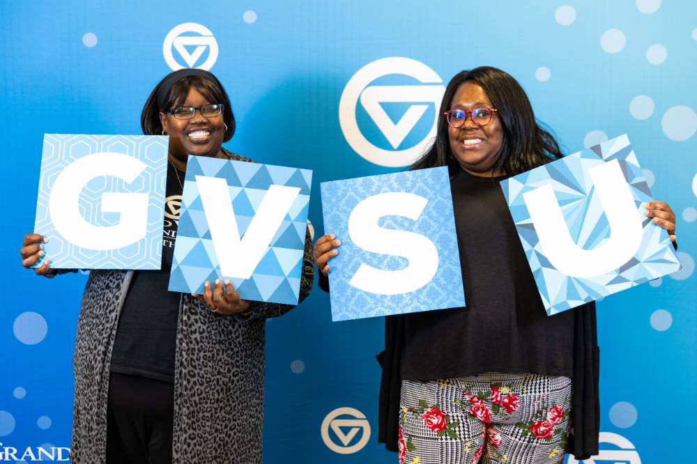 Mentors taking photos at the photobooth with GVSU sign